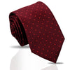 A deep red patterned silk necktie rolled and displayed on a reflective surface.