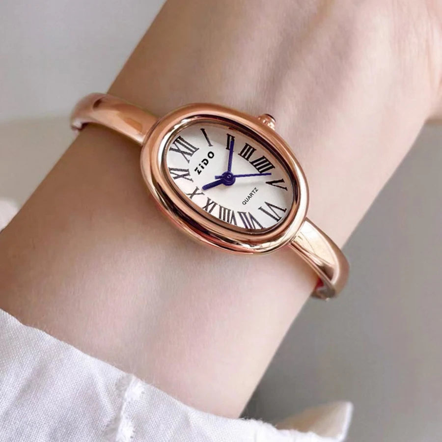 A close-up of a rose gold Zido quartz analog watch with an oval face worn on a wrist.