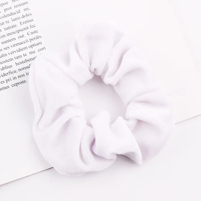 A close-up of a white velvet scrunchie, soft elastic hair tie, shown on a piece of paper.