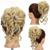 A woman's head showing a voluminous blonde hair bun styled with loose curls and a matching hair accessory.
