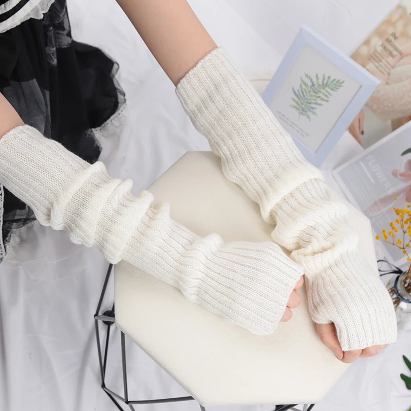A pair of cream-colored knitted fingerless gloves are displayed on a white surface.