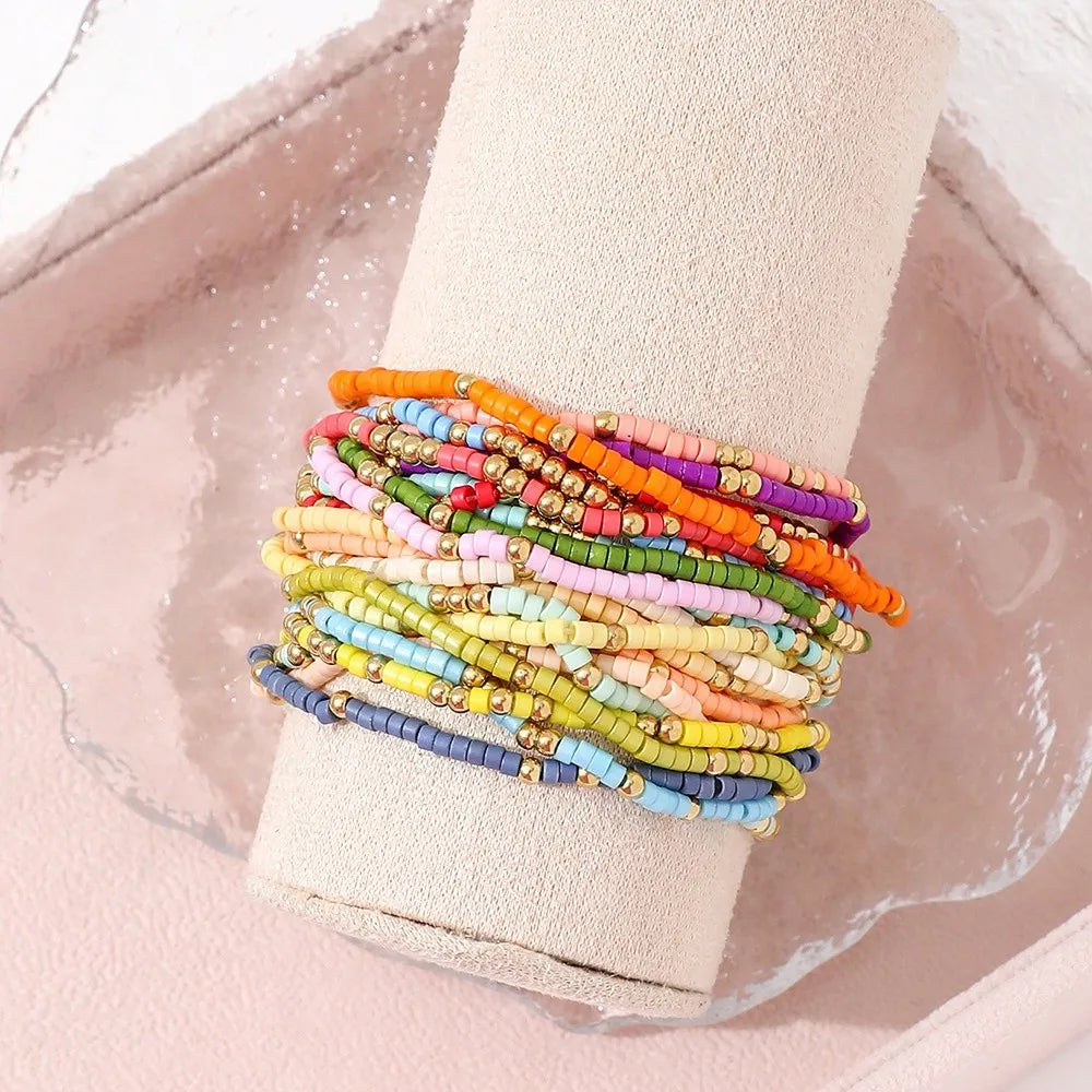 A stack of colorful beaded bangles is displayed on a light pink fabric background.