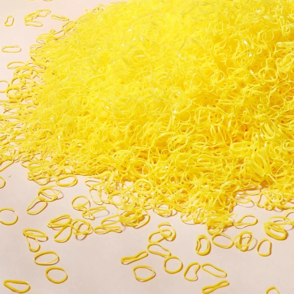 A pile of bright yellow disposable rubber hair ties for kids scattered on a white surface.