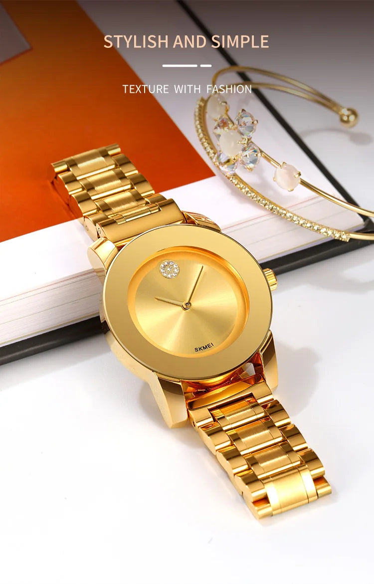 A gold minimalist quartz wristwatch with a round face and diamond accent, displayed on a white background.
