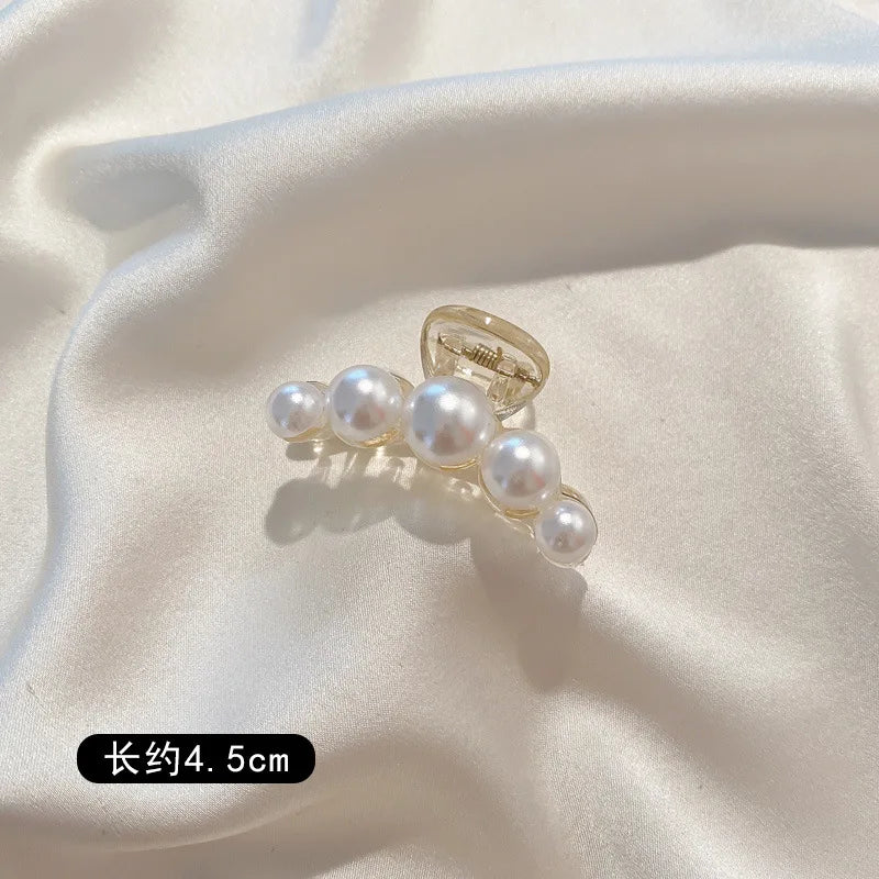 A set of simulated pearl hair claws displayed on a white satin fabric.