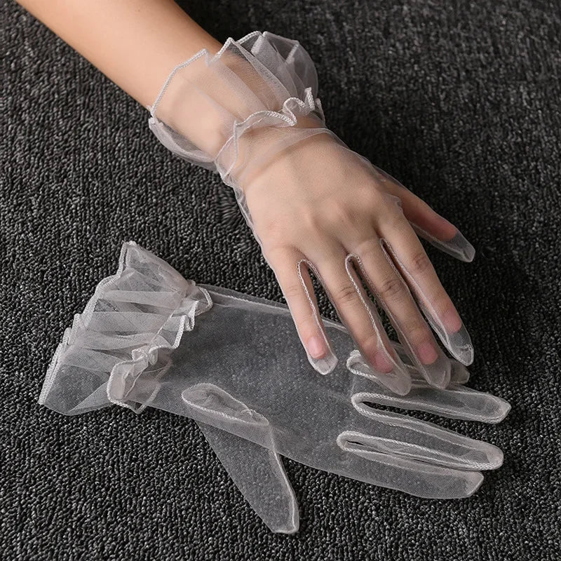 Clear lace tulle finger gloves worn on a hand against a dark gray fabric background.