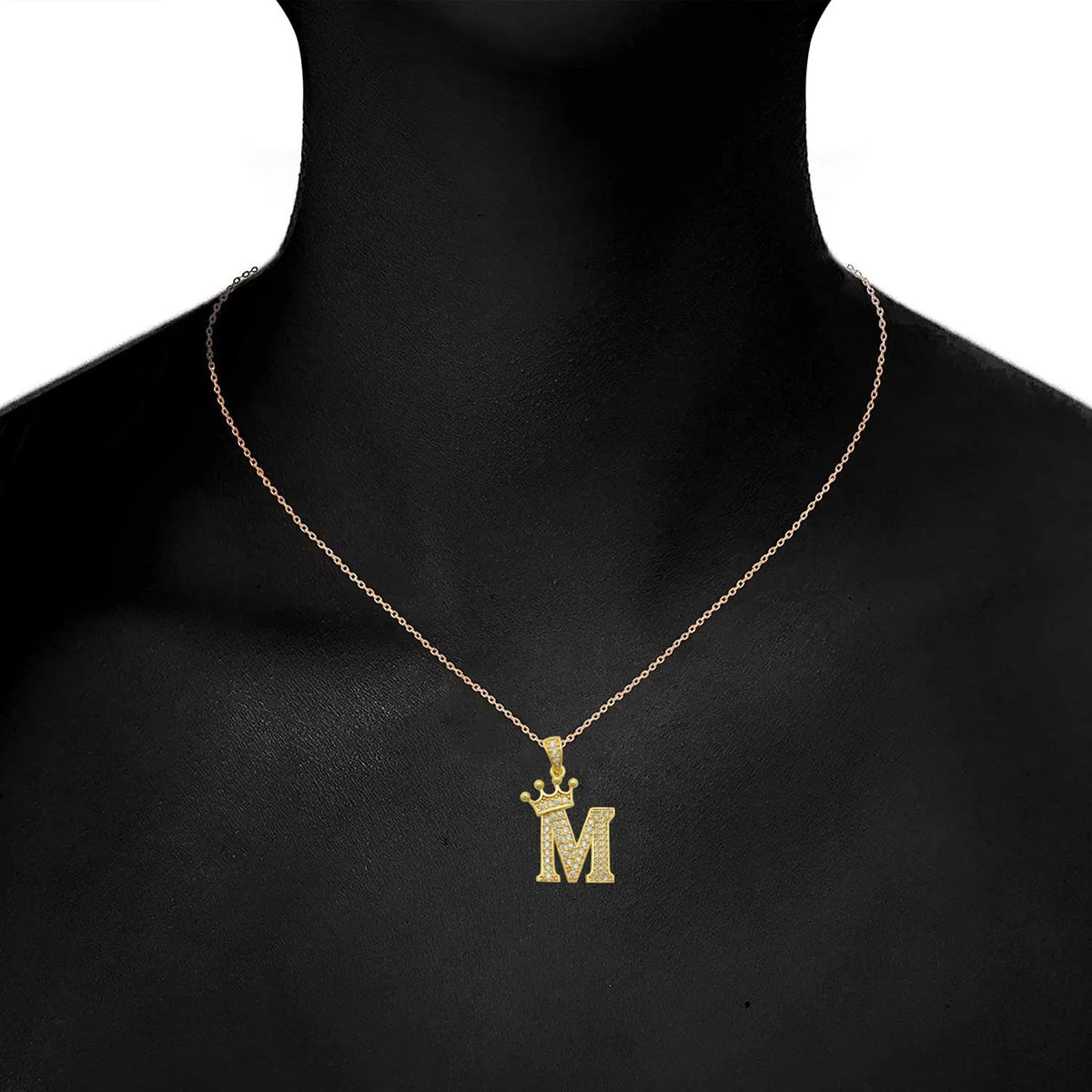 Gold initial M crown pendant necklace displayed on a black background
