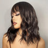 A woman with dark wavy hair is shown wearing a short bob wig against a light gray background.