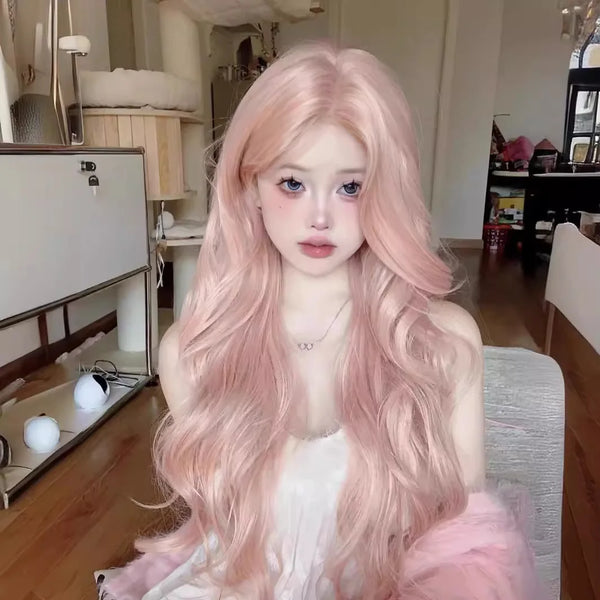 A woman with long, flowing rose pink synthetic hair wig is seated indoors.