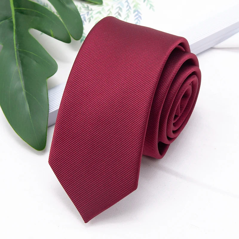 A deep burgundy men's slim jacquard business tie rolled and displayed next to a green leaf.