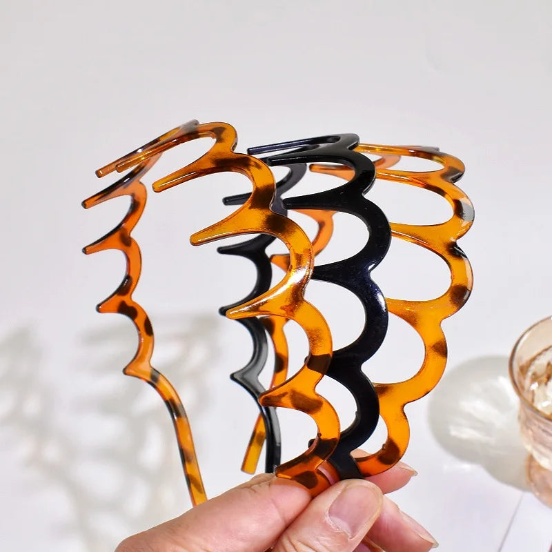 A hand holds a set of textured hair bands in shades of orange and black.