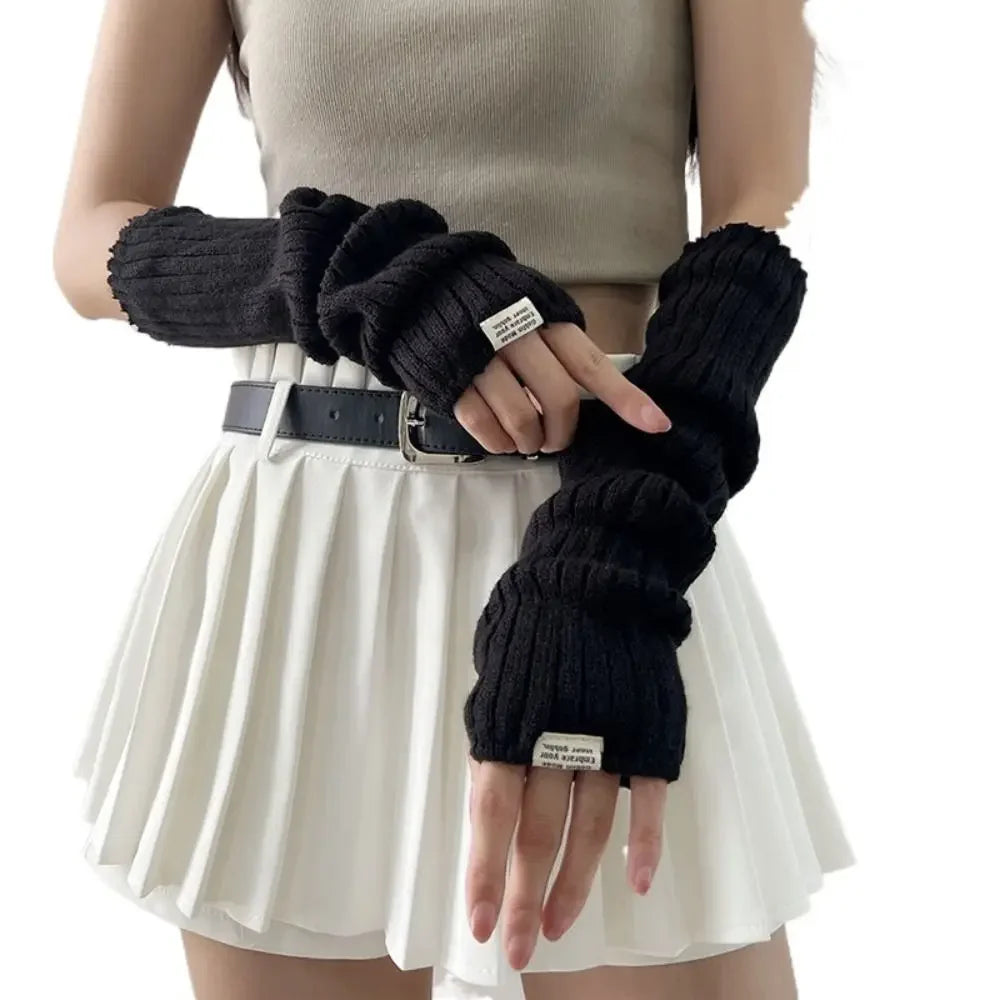 A woman wearing a beige top and white skirt is modeling black fingerless arm warmers.