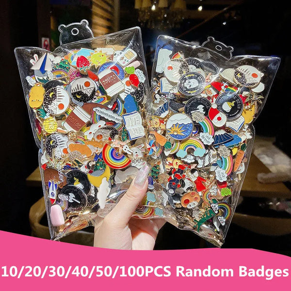 A hand holds two clear plastic bags filled with 100 random enamel badge pins and brooches.
