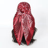 A deep red satin silk scarf featuring white paisley and polka dot patterns tied around dark hair.