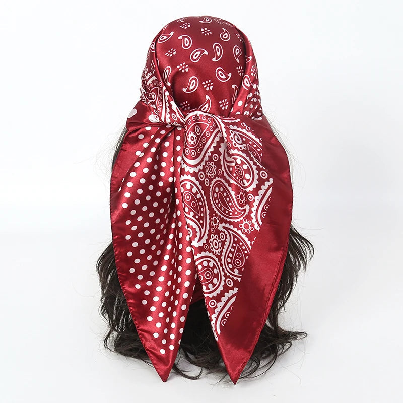 A deep red satin silk scarf featuring white paisley and polka dot patterns tied around dark hair.