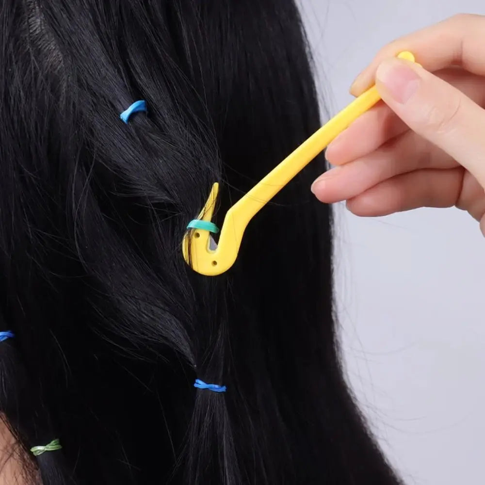 A hand is using a yellow tool to remove an elastic or rubber band from black hair.