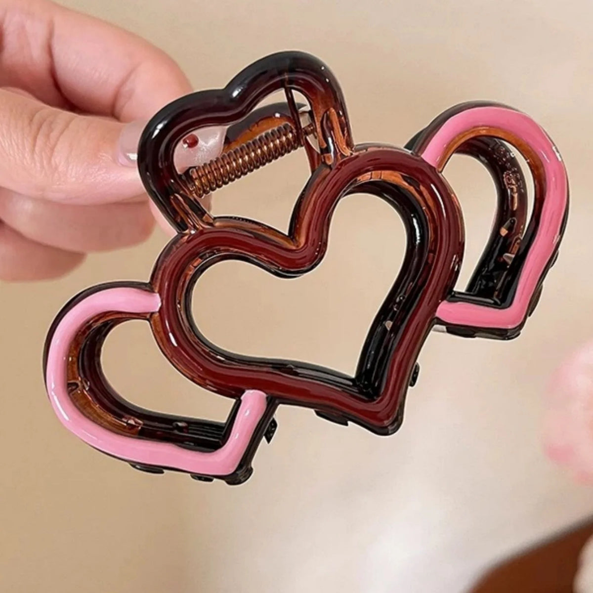 A hand holds a heart-shaped hair claw with dark brown and pink translucent plastic.