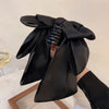A black satin bow hair clip is shown being used to secure a ponytail.
