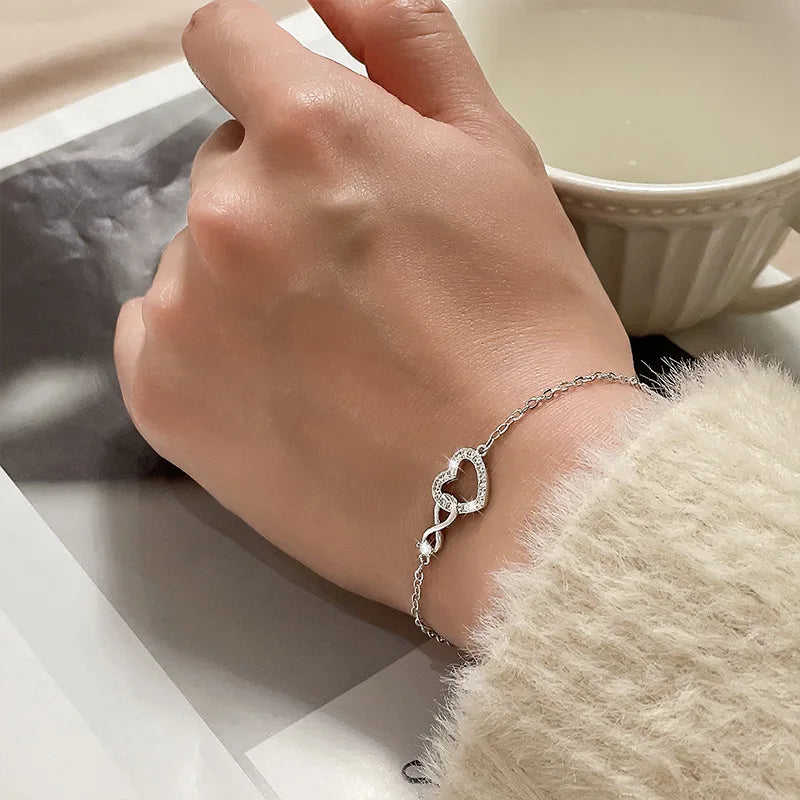 A close-up of a hand wearing a sterling silver double heart charm bracelet next to a white ceramic cup.
