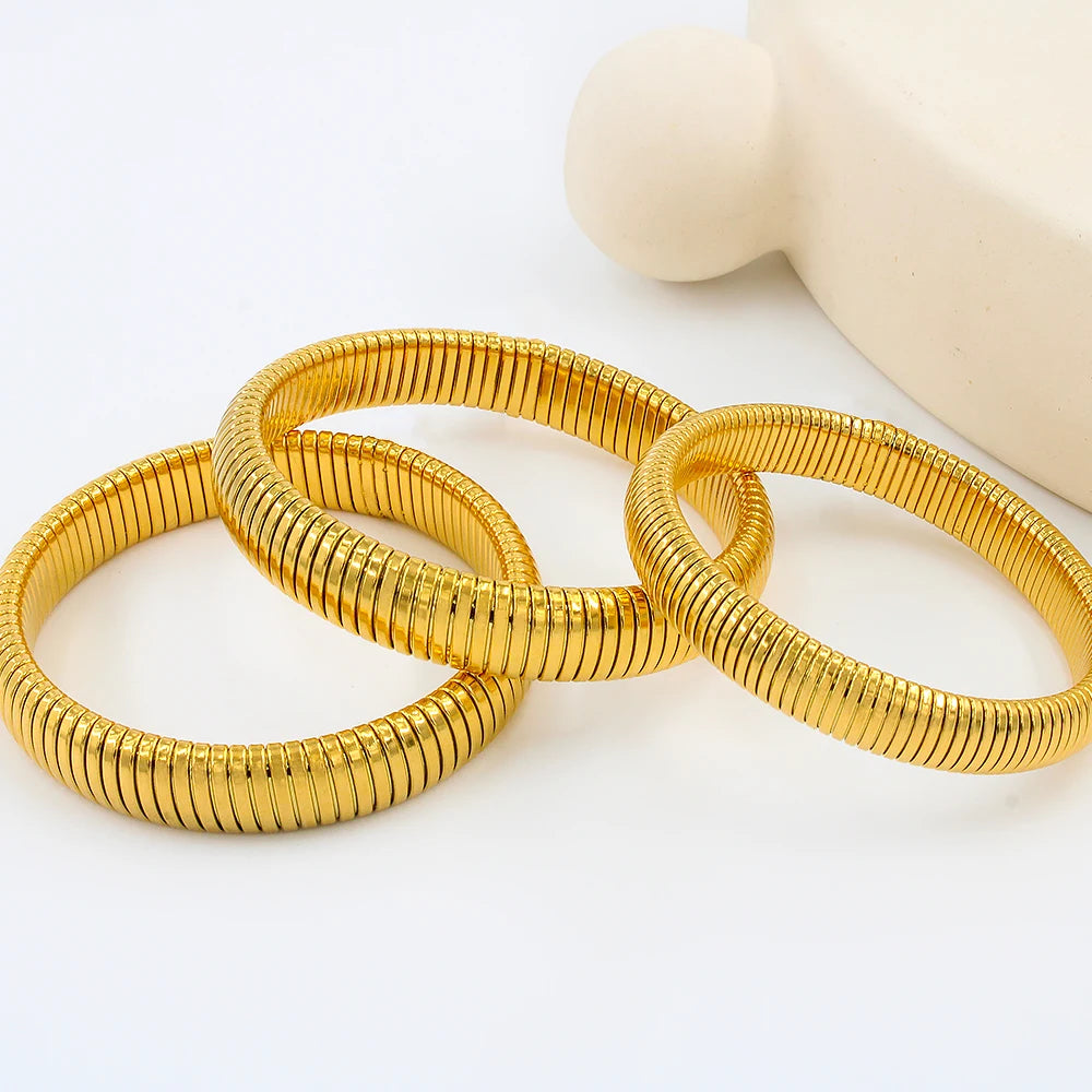 Three stacked gold-colored elastic bangle bracelets resting on a white surface.