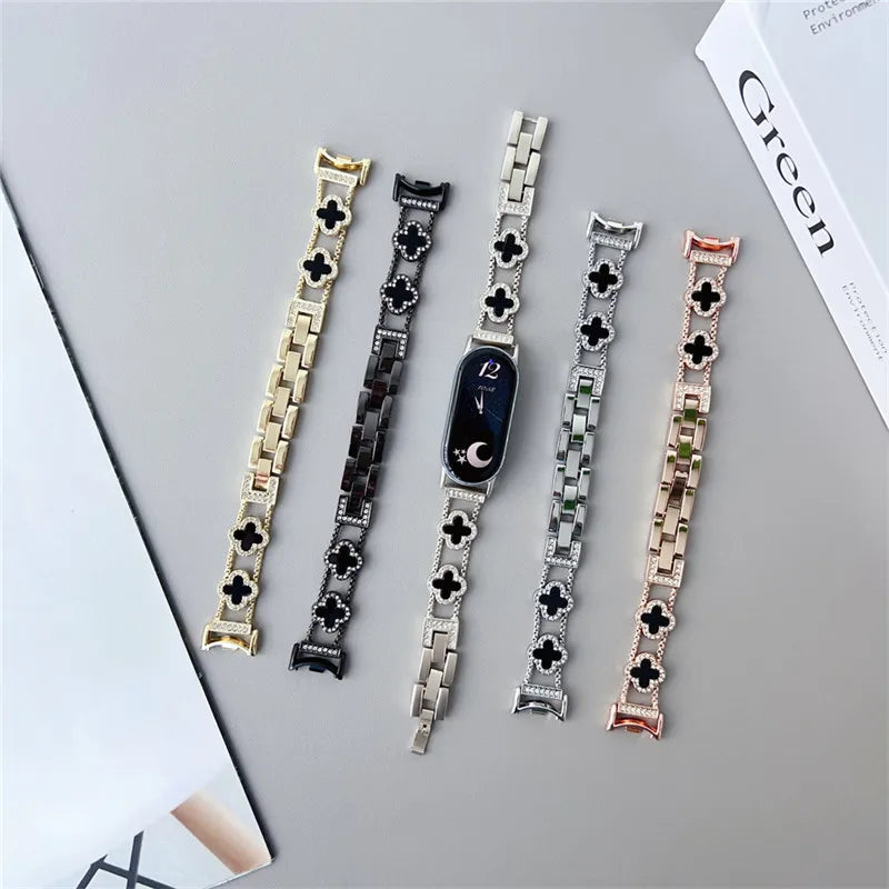A collection of five diamond four-leaf clover watch straps for a Xiaomi Mi Band displayed on a gray surface.