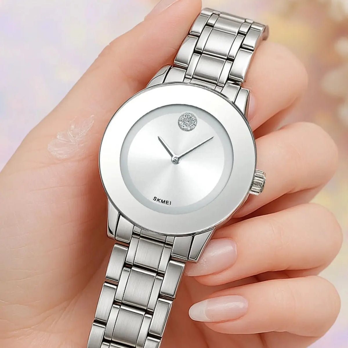 Primer plano de un reloj de cuarzo plateado con pulsera de eslabones metálicos siendo sostenido por una mano.