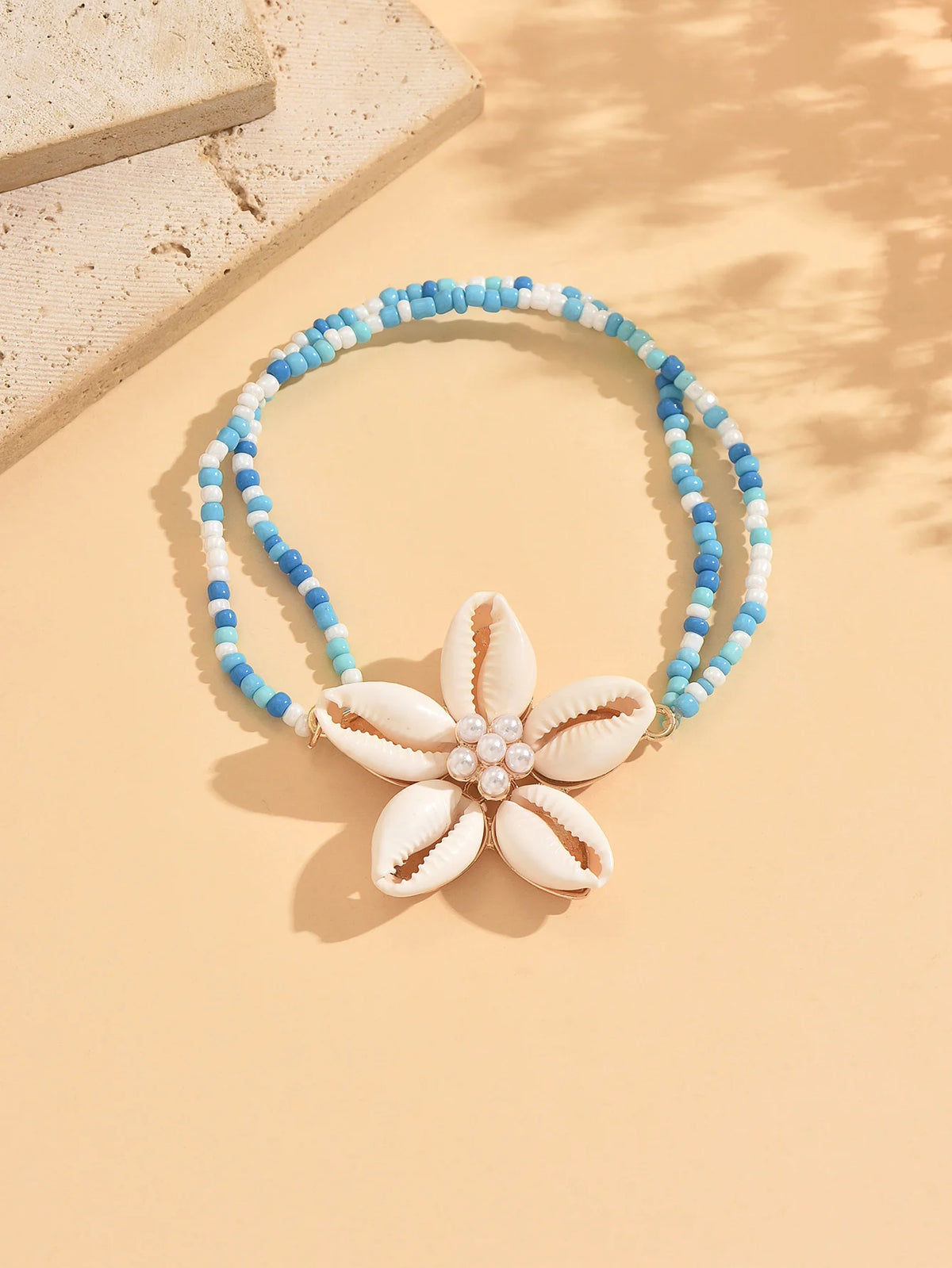 A beaded bracelet featuring white and blue cowrie shells with a floral charm.