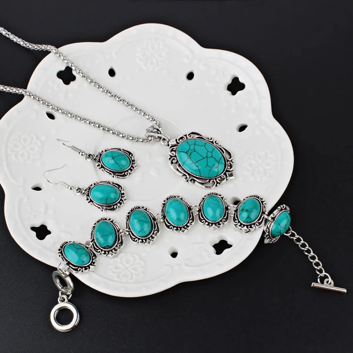 Silver jewelry set featuring turquoise stones including a necklace, earrings, and bracelet displayed on a white tile