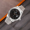 A silver-toned men's wristwatch with a black dial and a metal bracelet is shown on a gray background.