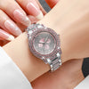 A silver watch with a pink dial and rose gold accents is worn on a wrist, displayed next to manicured hands.