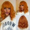 A woman models a short wavy bob wig in bright orange hair against a light background.