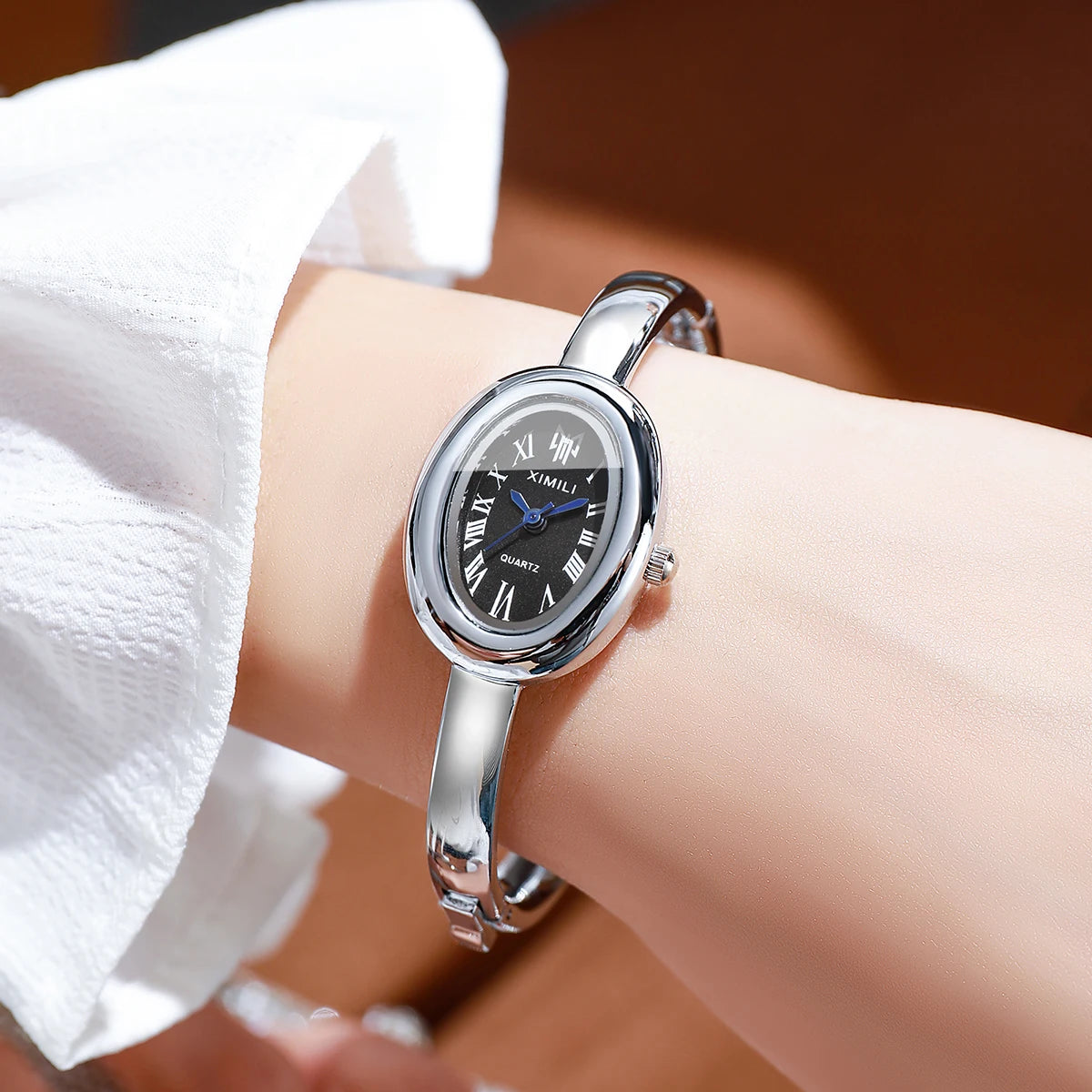A close-up of a silver quartz watch bracelet worn on a wrist, with a white shirt sleeve visible.