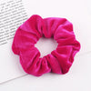 A close-up photo of a bright pink velvet scrunchie, showing its gathered texture and soft fabric.