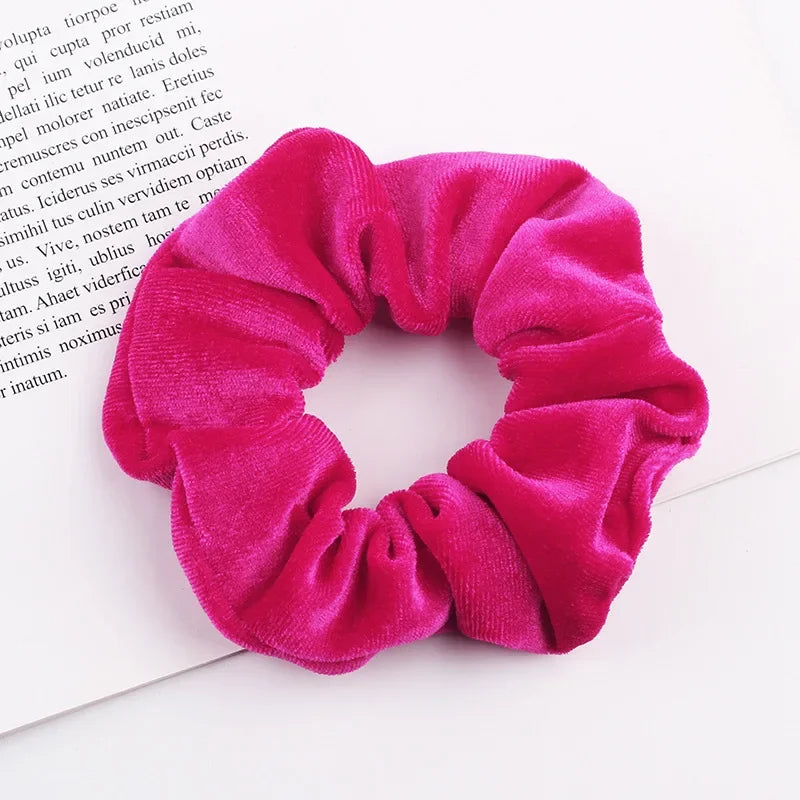 A close-up photo of a bright pink velvet scrunchie, showing its gathered texture and soft fabric.