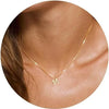 A close-up of a gold plated alphabet initial necklace resting on a person's neck and collarbone.