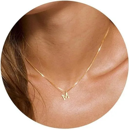 A close-up of a gold plated alphabet initial necklace resting on a person's neck and collarbone.