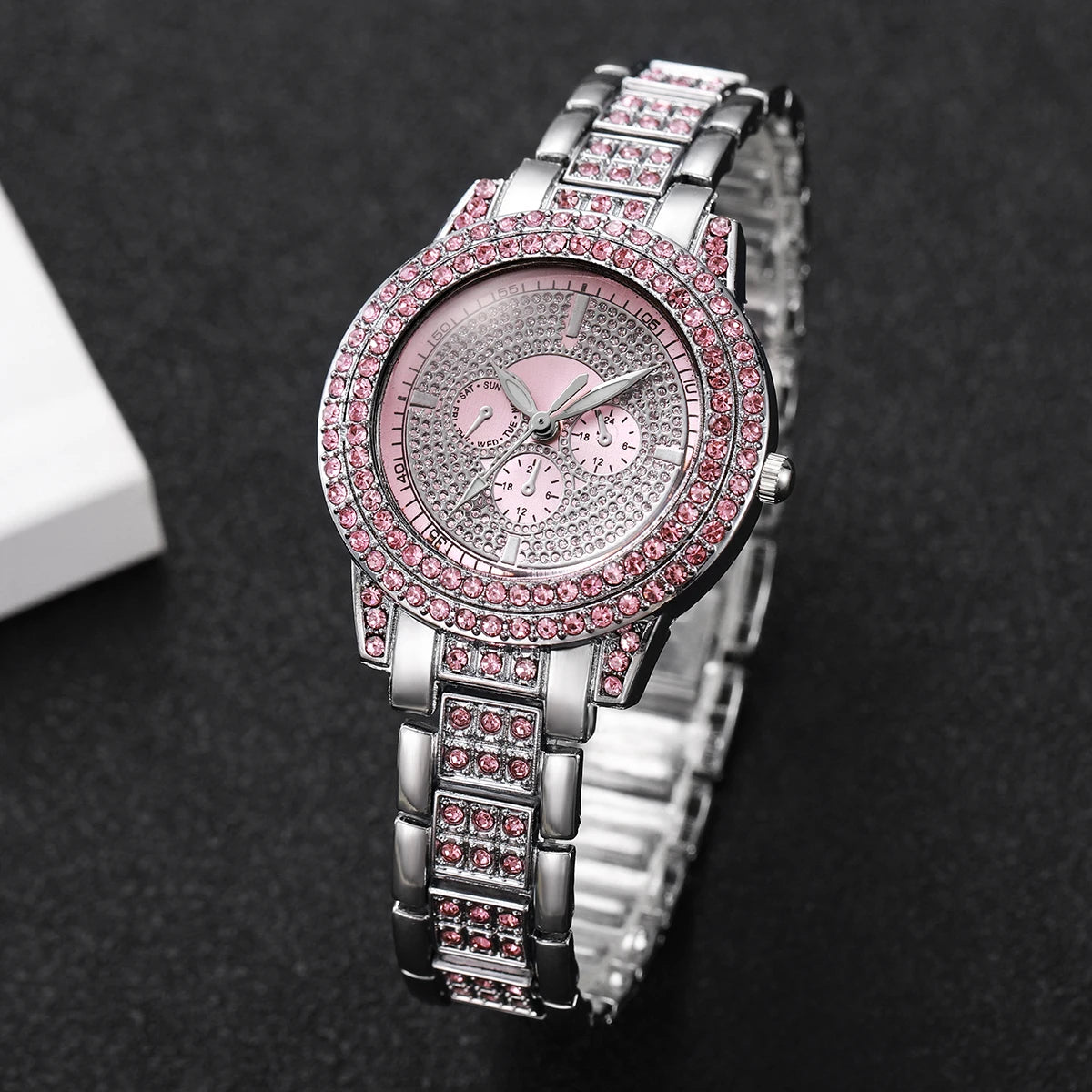 A silver watch with a pink diamond rhinestone bezel and bracelet set against a dark background.