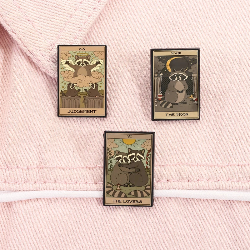 A set of three tarot card enamel pins featuring Judgement, The Moon, and The Lovers on a pink fabric background.