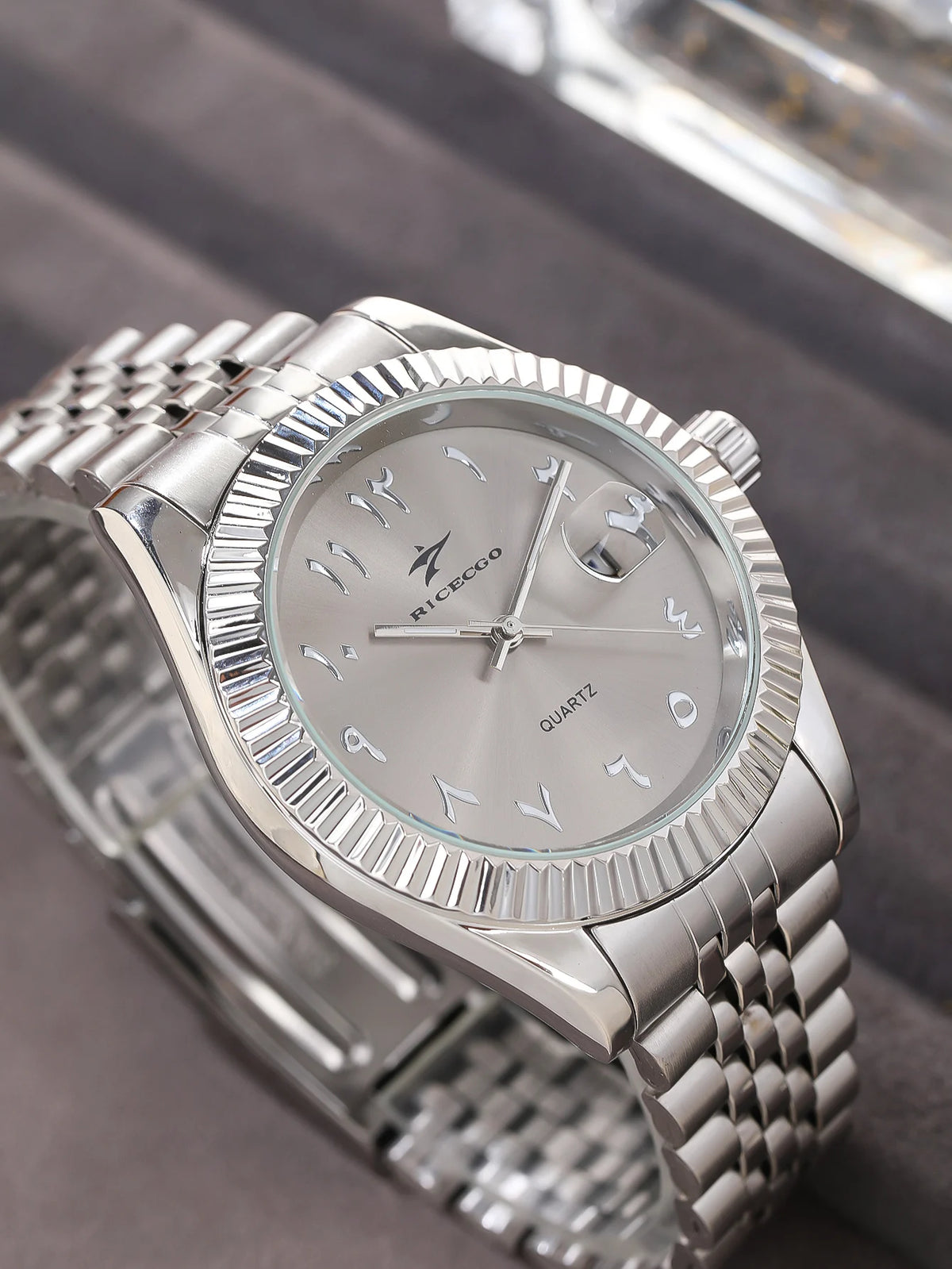 A silver luxury quartz men's wristwatch with a metal bracelet and a date display, shown on a dark surface.