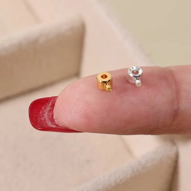 A close-up of a finger showing gold and silver jewelry findings stoppers or spacers on the fingertip.
