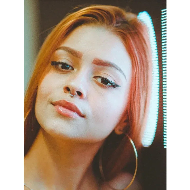 A close-up portrait of a woman wearing a silver nose ring and septum piercing.