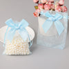 A light blue organza drawstring gift bag tied with a bow, filled with pink flowers and white pearls.