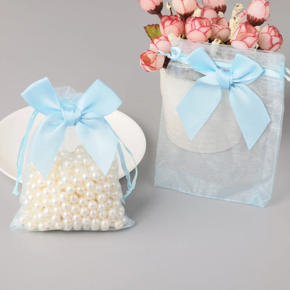 A light blue organza drawstring gift bag tied with a bow, filled with pink flowers and white pearls.