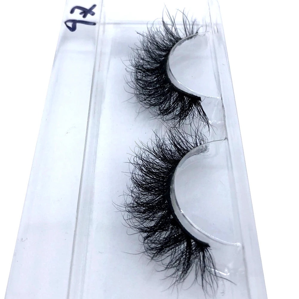 A pair of natural mink false eyelashes displayed on a clear plastic slide.