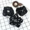 A set of three black fabric scrunchie headbands with various textures and patterns displayed on a white plate.