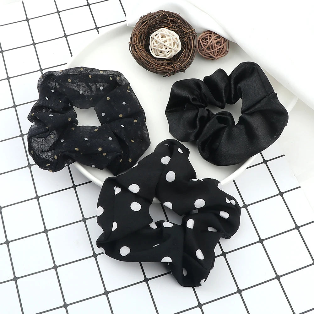 A set of three black fabric scrunchie headbands with various textures and patterns displayed on a white plate.