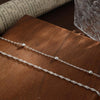 Two delicate gold-plated twisted ankle bracelets laid on a dark wooden surface.