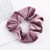 A close-up shot of a set of six dusty rose velvet scrunchies for hair ties lying on white paper.