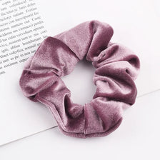 A close-up shot of a set of six dusty rose velvet scrunchies for hair ties lying on white paper.