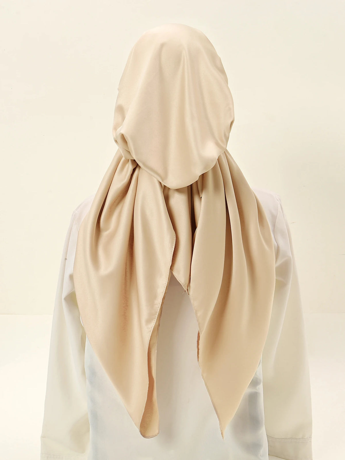 A beige satin silk hijab is draped around a person's head and neck.